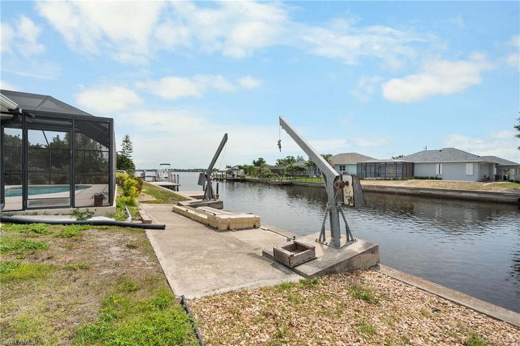 Waterfront property featuring a canal with boat lifts, concrete seawall, and screened-in pool enclosure