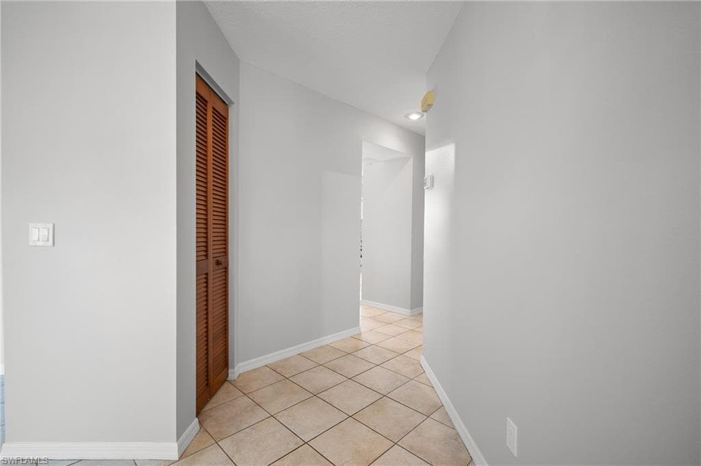 Hallway featuring diagonal tile flooring, white baseboards, light gray wall paint, and a louvered bifold door