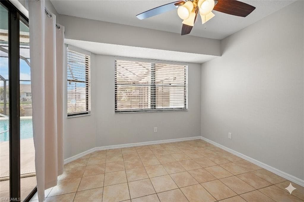 Tiled flooring room with multiple windows, a ceiling fan, and sliding glass doors revealing a screened pool enclosure