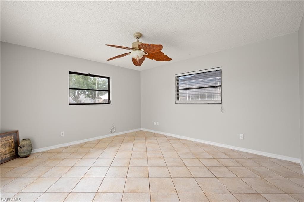 Neutral-toned room featuring a ceiling fan with wood-finish blades, two windows with black frames, and light-colored tile flooring