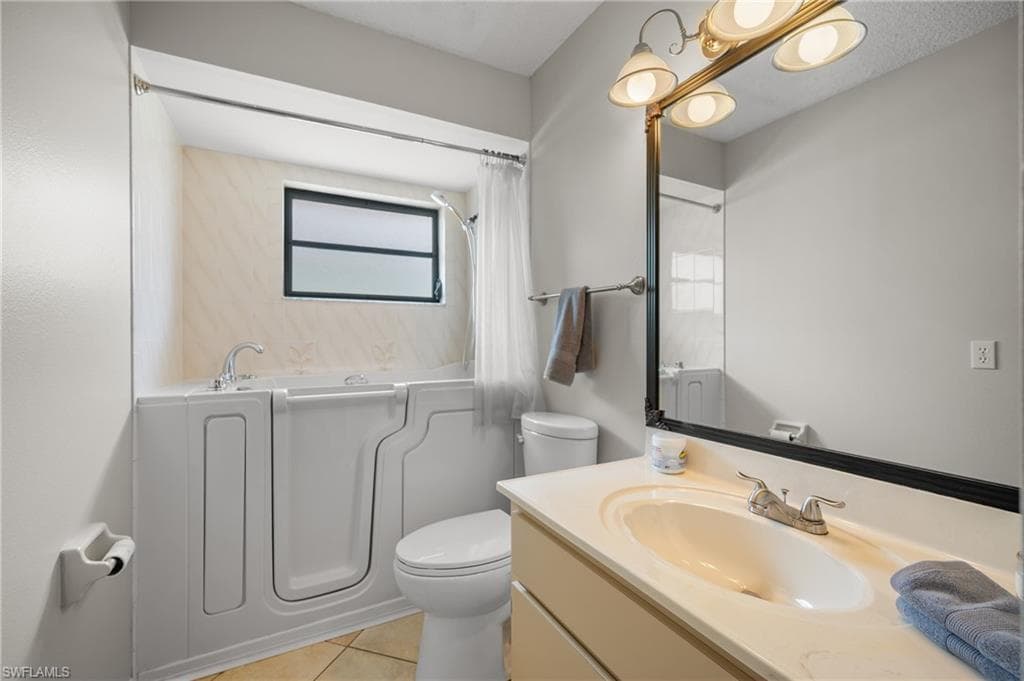 Bathroom featuring a walk-in tub with a shower attachment, a single vanity with an integrated sink, a large mirror, and tiled flooring
