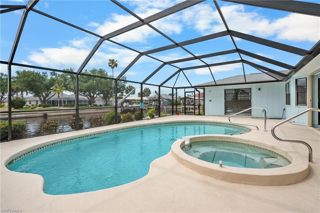 Screened lanai featuring a freeform swimming pool with integrated spa, spacious pool deck, and direct water access
