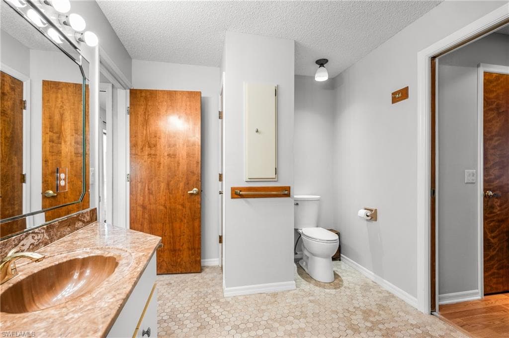 Bathroom featuring a vanity with a patterned countertop and integrated sink, a large wall mirror with overhead lighting, hexagon tile flooring, light gray wall paint, and a built-in wall cabinet