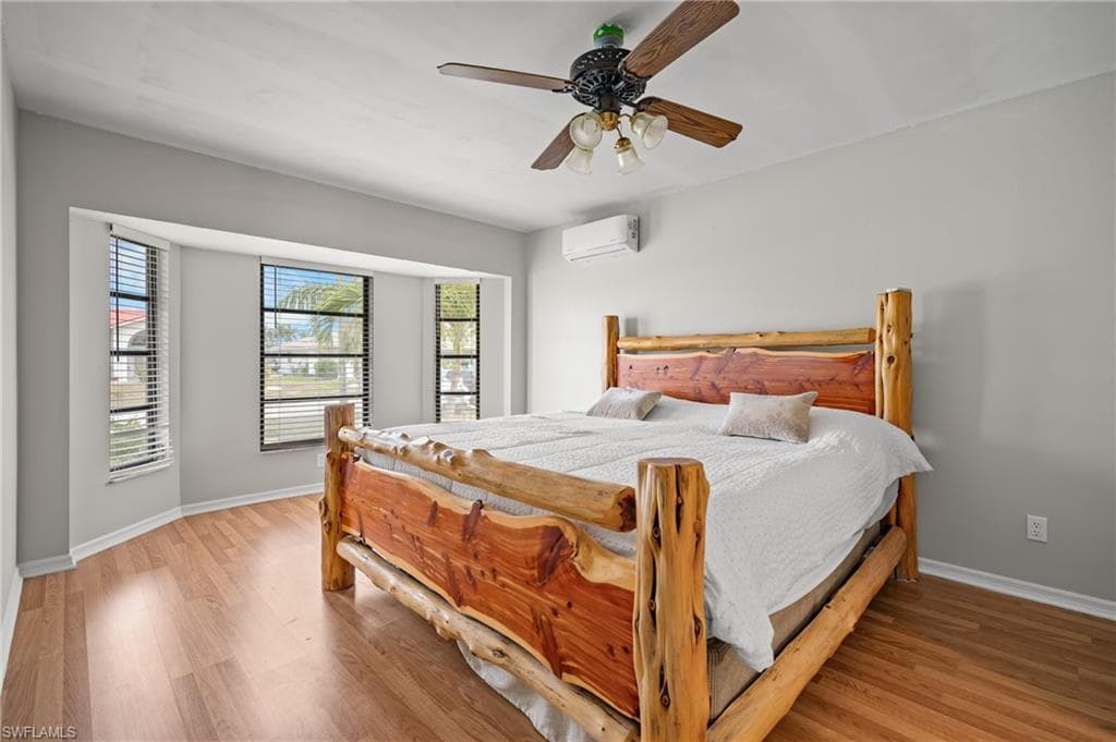 Bay window with multiple windows, wood-finish flooring, ceiling fan with light fixture, and a wall-mounted mini-split unit