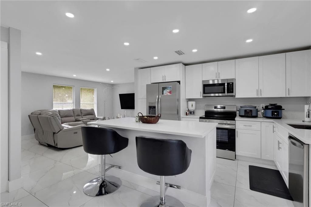 Kitchen with white cabinetry, stainless steel appliances, and a central island with countertop seating