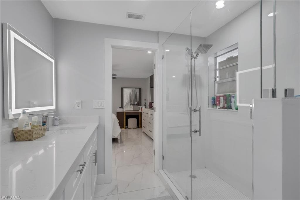 Bathroom featuring a glass-enclosed shower with a rainfall showerhead, a window with horizontal blinds, and a vanity with a quartz countertop and an illuminated mirror
