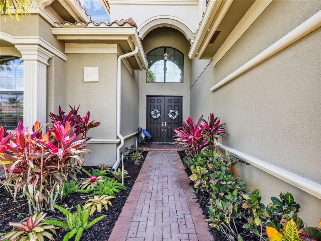 Arch-top double entry doors with decorative glass transom, flanked by vibrant landscaping and a brick paver walkway