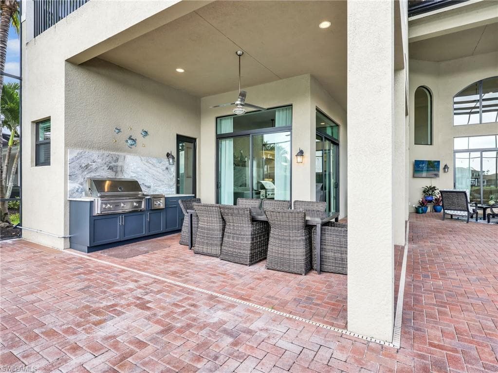 Covered outdoor patio featuring a built-in stainless steel grill with a marbled backsplash, recessed lighting, and a ceiling fan