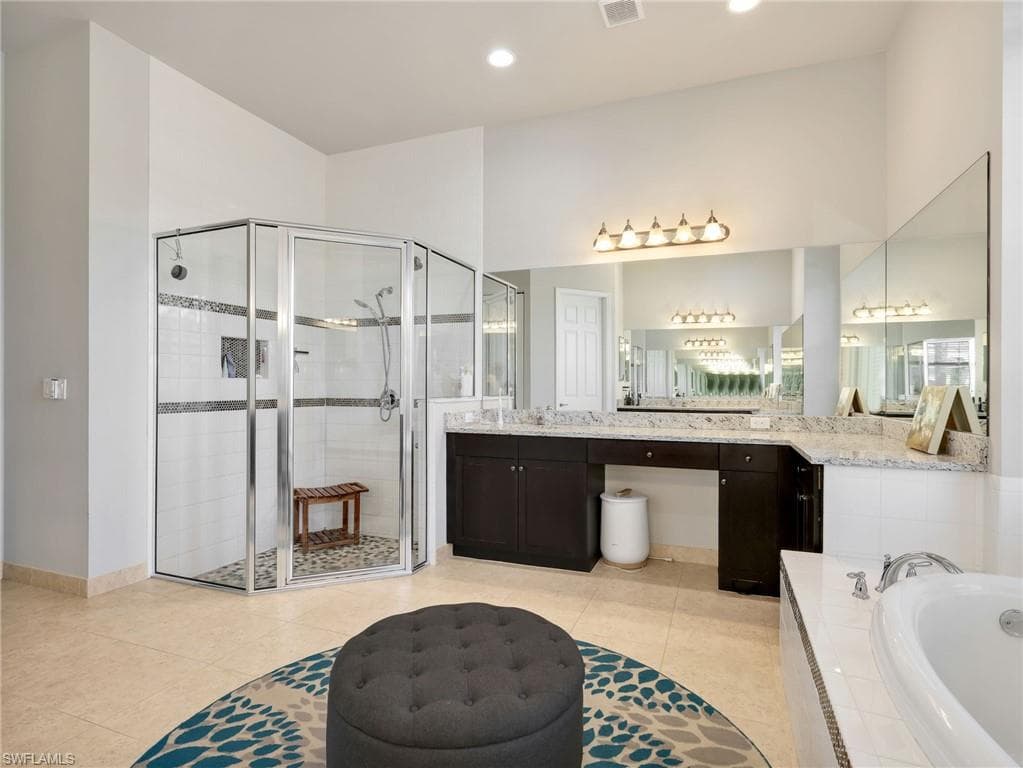 Spacious bathroom featuring a glass-enclosed shower with tile surround, a built-in soaking tub, extensive vanity with dual sinks and stone countertop, and large wall-mounted mirrors