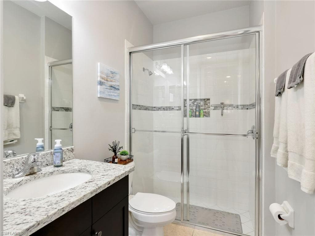 Bathroom featuring a glass-enclosed shower with tile surround and decorative accent band, a white toilet, and a vanity with a white-patterned countertop and undermount sink