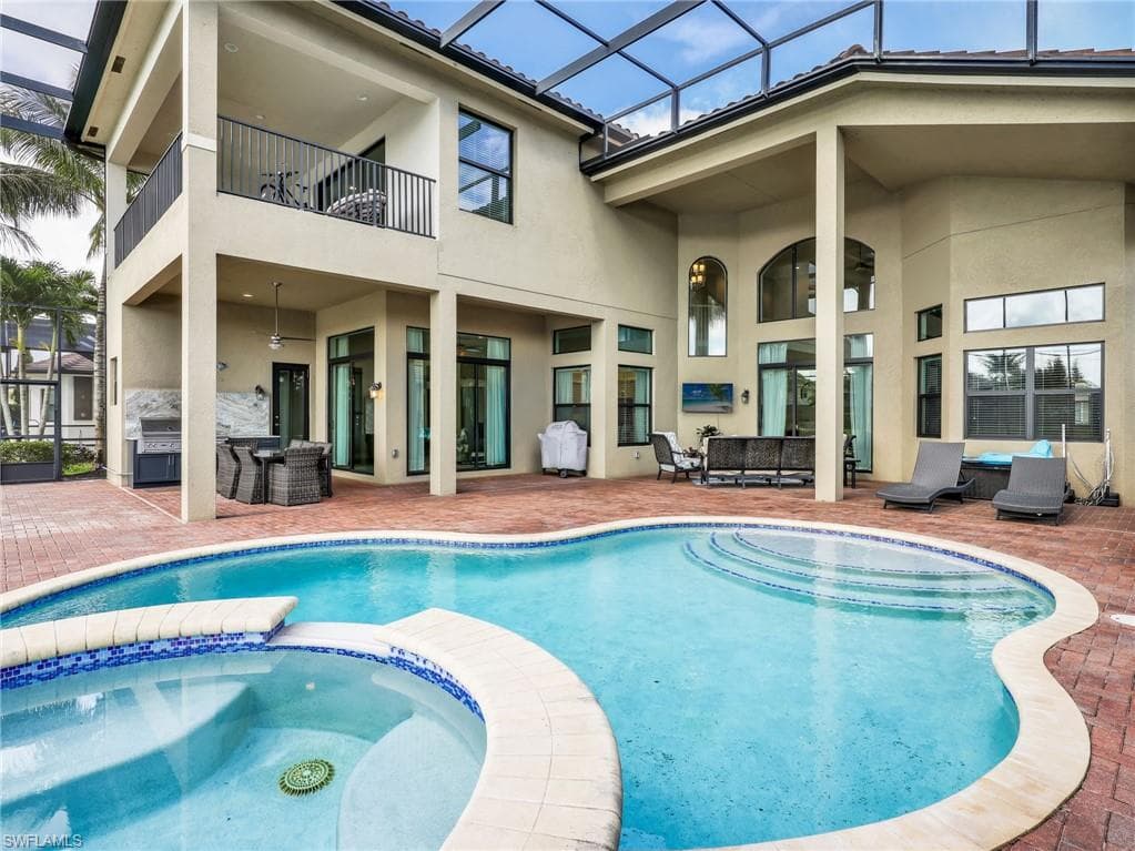 Expansive brick paver patio featuring a free-form pool with integrated spa and a screened enclosure