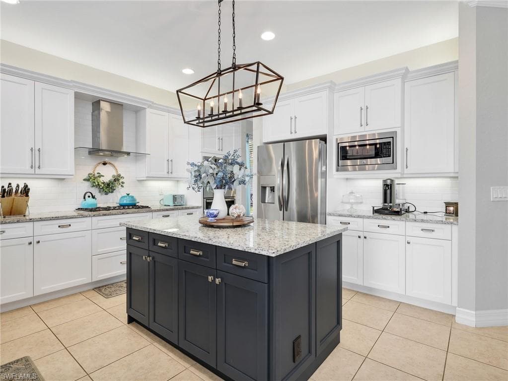 Kitchen featuring a dark-toned island with ample storage, light-toned perimeter cabinetry, stainless steel appliances, granite countertops, and a white subway tile backsplash