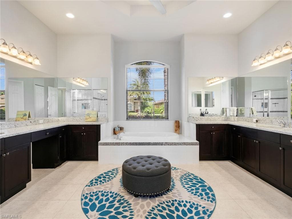 Spacious Master bathroom featuring a built-in soaking tub, dual vanities with stone countertops, dark wood-finish cabinetry, and tile flooring