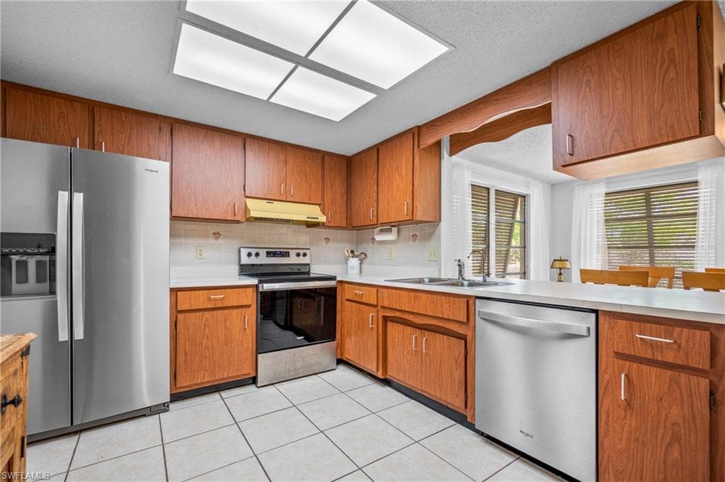 Kitchen featuring wood cabinetry, white countertops, tile flooring, and stainless steel appliances including a side-by-side refrigerator, range, and dishwasher