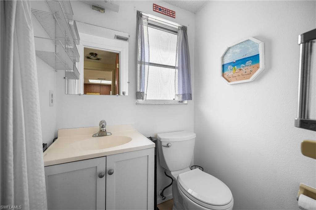 Bathroom featuring a white toilet, single vanity with light-colored countertop, and integrated sink