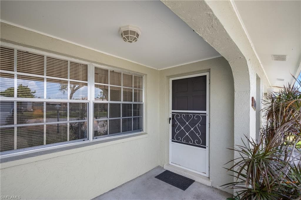Covered entryway featuring a decorative screen door, multi-pane windows with blinds, and a smooth concrete floor