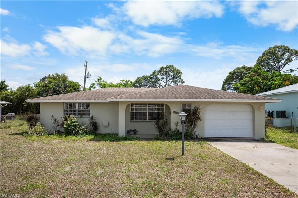 Single-story residence featuring a neutral stucco exterior, a shingled roof, an attached garage with a white door, and a concrete driveway