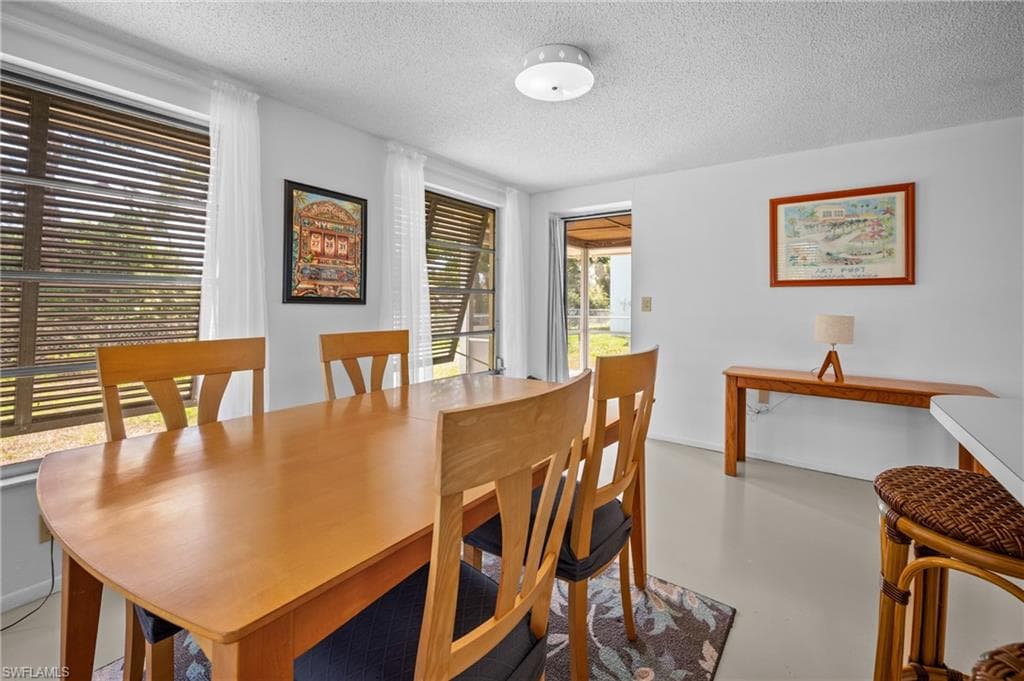 Bright dining area featuring multiple windows with blinds, a ceiling-mounted light fixture, and direct access to an outdoor screened enclosure