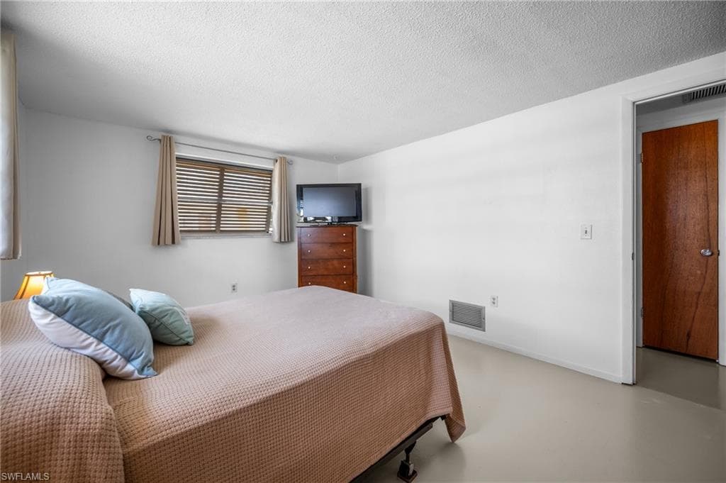 Bedroom featuring light-toned flooring, a window with horizontal blinds and drapes, and a solid wood interior door with a silver-tone handle
