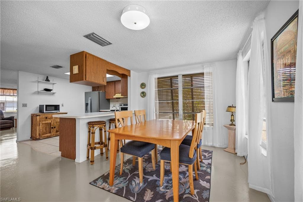 Open-concept living space featuring a dining area with a window, wood-finish flooring, a breakfast bar, and a kitchen with wood cabinetry