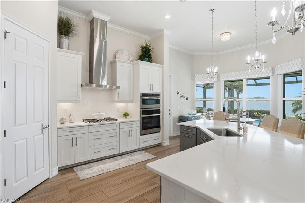 Kitchen featuring a large island with an undermount sink, pendant lighting, built-in double ovens, a gas cooktop with a stainless steel range hood, and wood-finish flooring