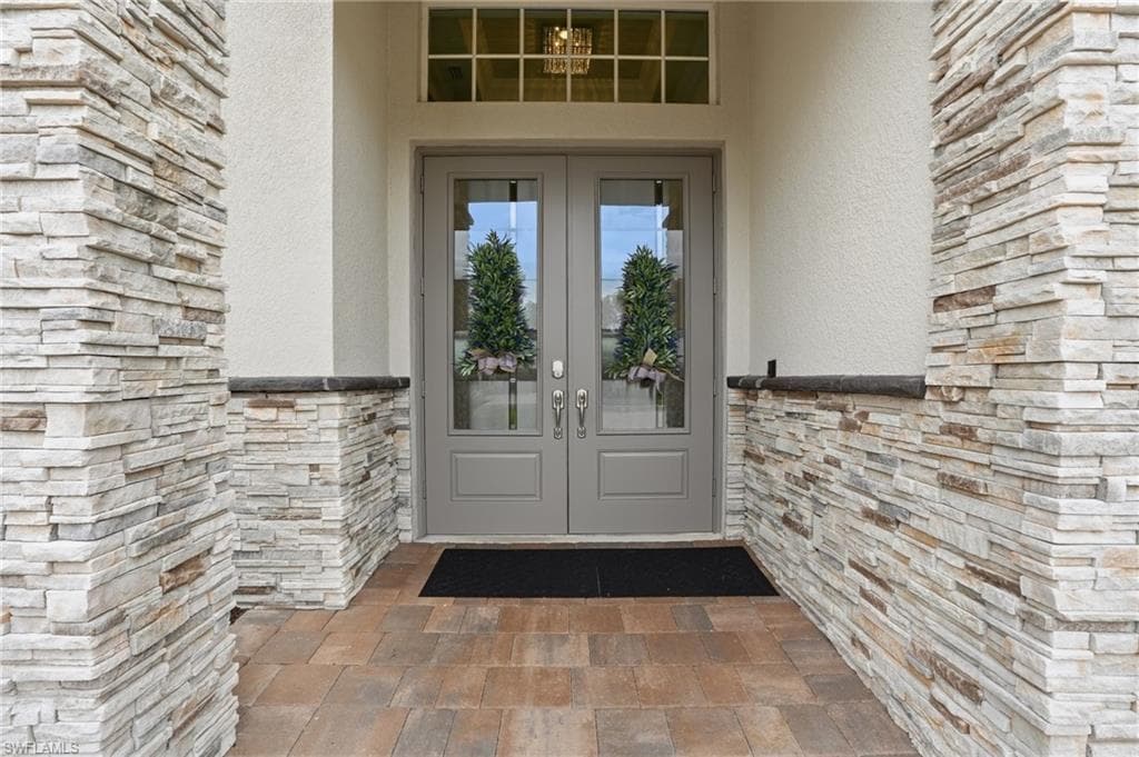 Stone veneer facade with stucco accents, double entry doors with integrated glass, transom window, and a paver stone porch