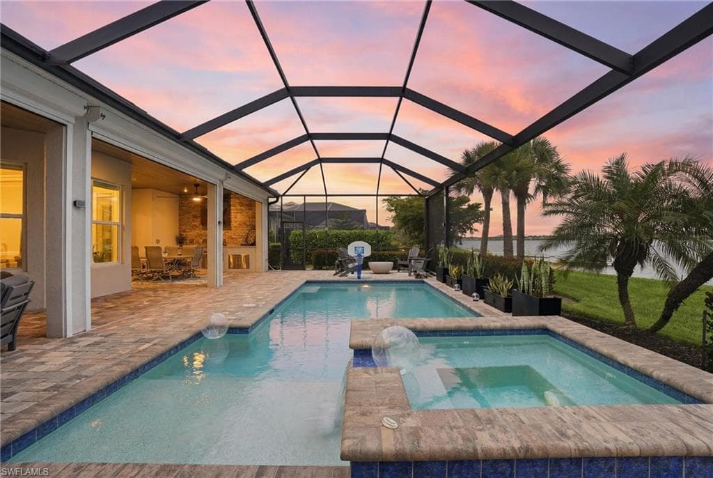 Screened outdoor living area featuring a pool with an integrated spa, expansive paver decking, and an outdoor kitchen