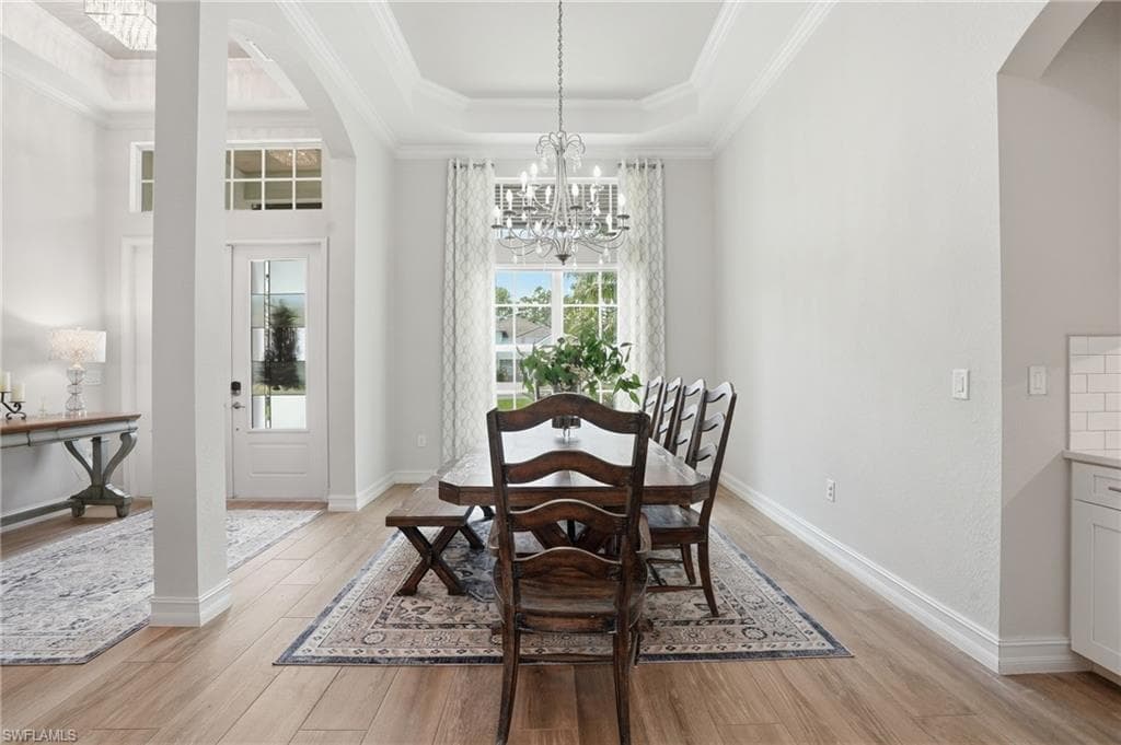 Formal dining area featuring wood-finish flooring, a tray ceiling with crown molding, and a chandelier