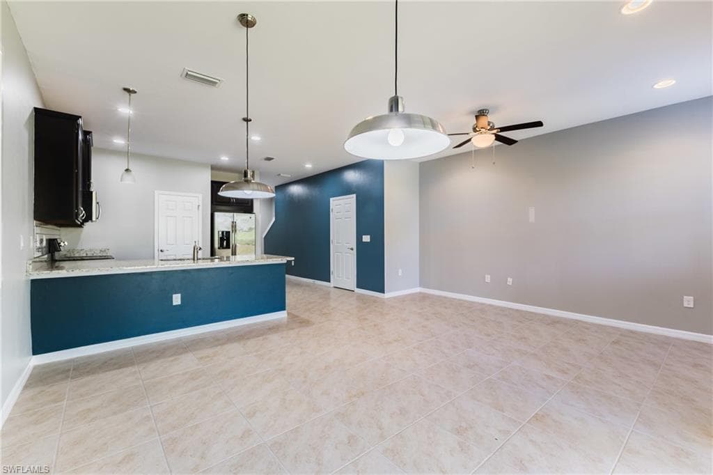 Kitchen featuring pendant lighting, light stone counters, stainless steel refrigerator with ice dispenser, and a ceiling fan