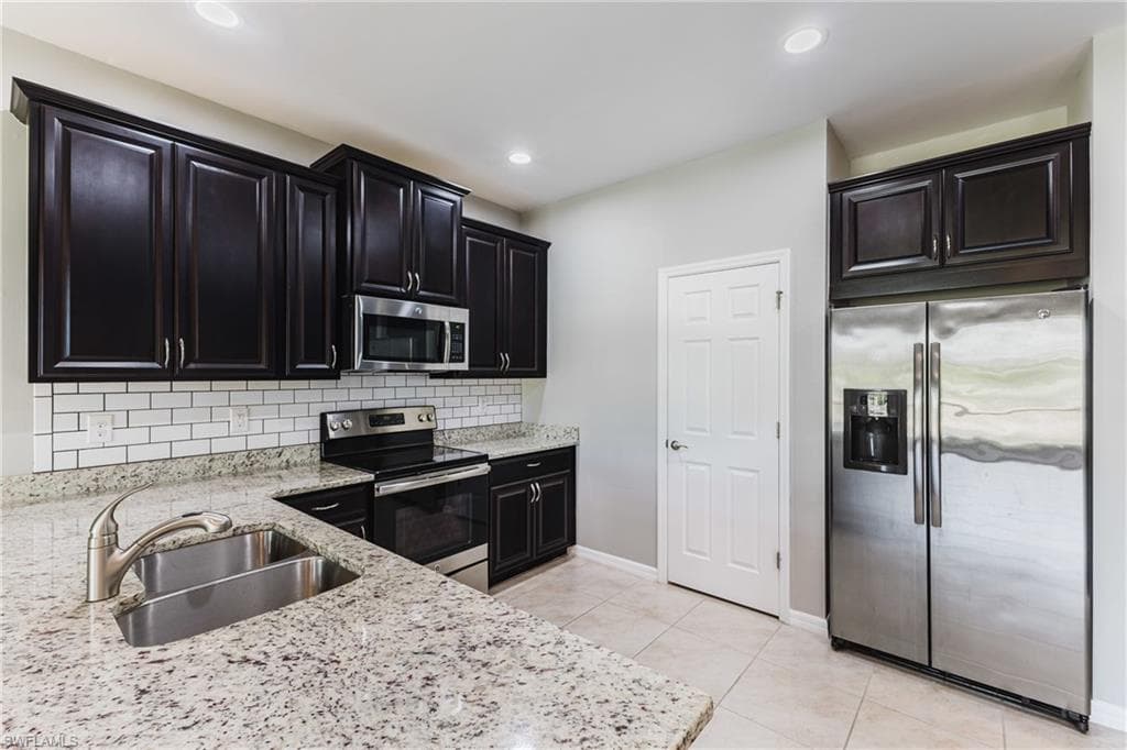 Kitchen with stainless steel appliances, light stone counters, dark cabinetry, light tile patterned floors, and decorative backsplash