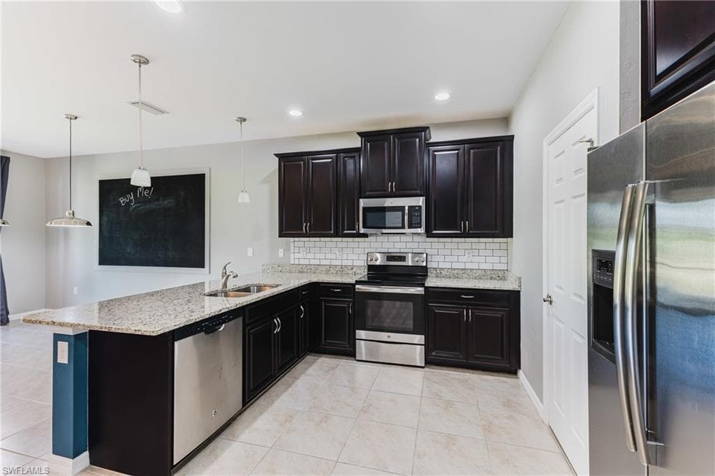 Kitchen featuring stainless steel appliances, hanging light fixtures, light stone countertops, dark cabinets, and a peninsula