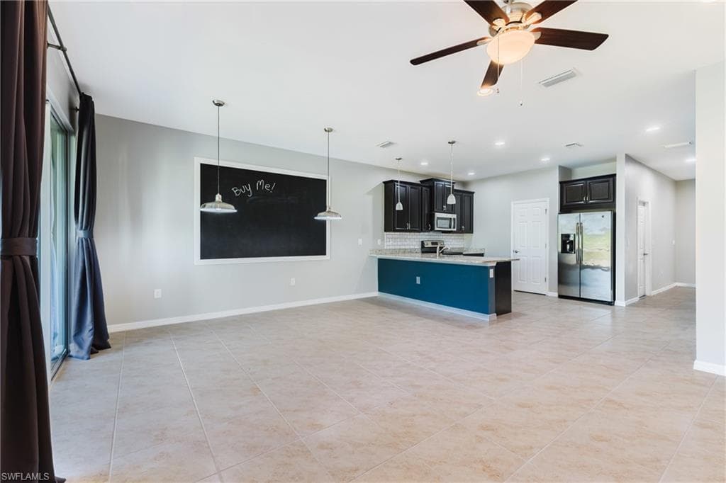 Kitchen with dark cabinetry, stainless steel appliances, open floor plan, a ceiling fan, and pendant lighting