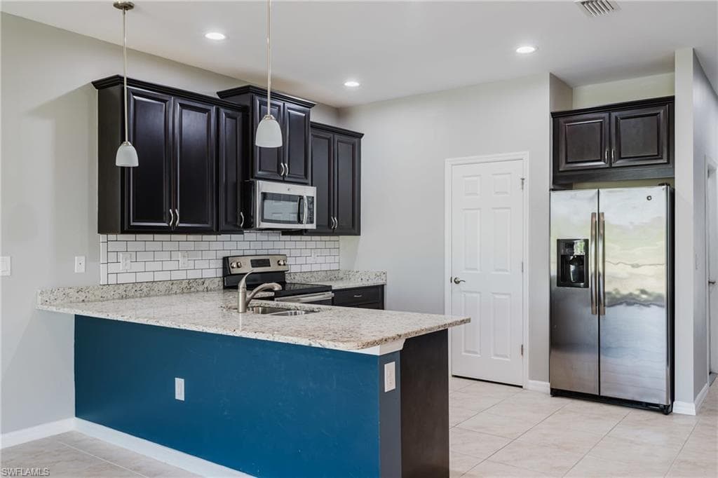 Kitchen featuring stainless steel appliances, a peninsula, hanging light fixtures, backsplash, and light stone counters