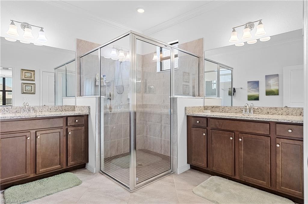 Full bath featuring ornamental molding, two vanities, a stall shower, and light tile patterned floors
