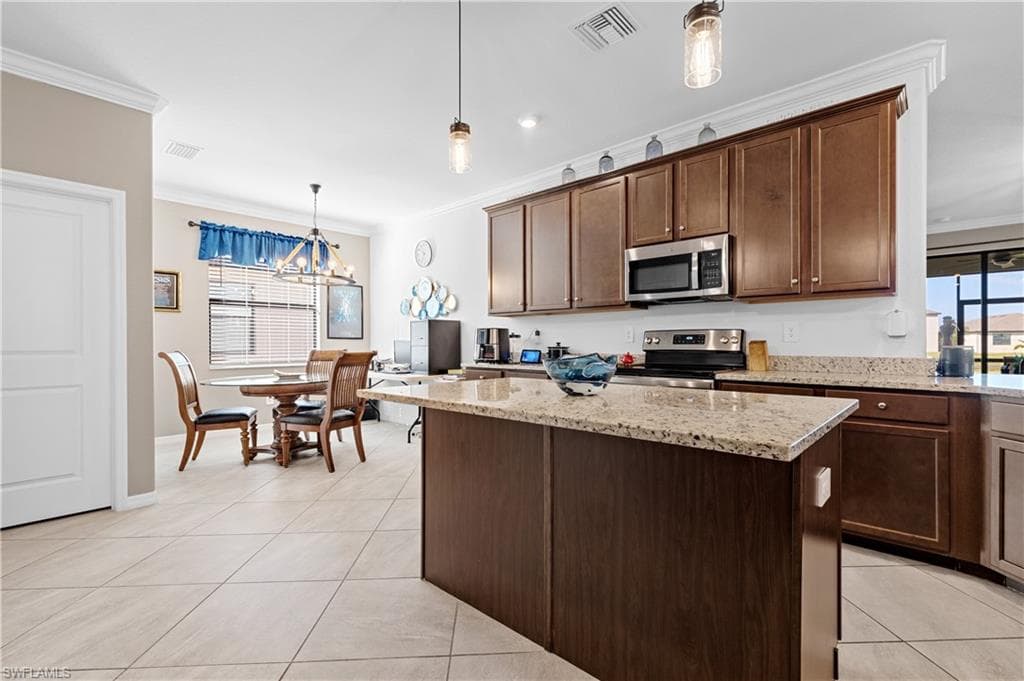 Kitchen with stainless steel appliances, hanging light fixtures, dark brown cabinetry, crown molding, and light tile patterned floors