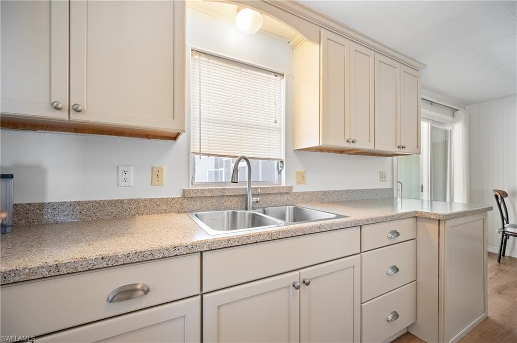 Kitchen featuring light-toned cabinetry, speckled countertops, a double basin stainless steel sink, and a gooseneck faucet