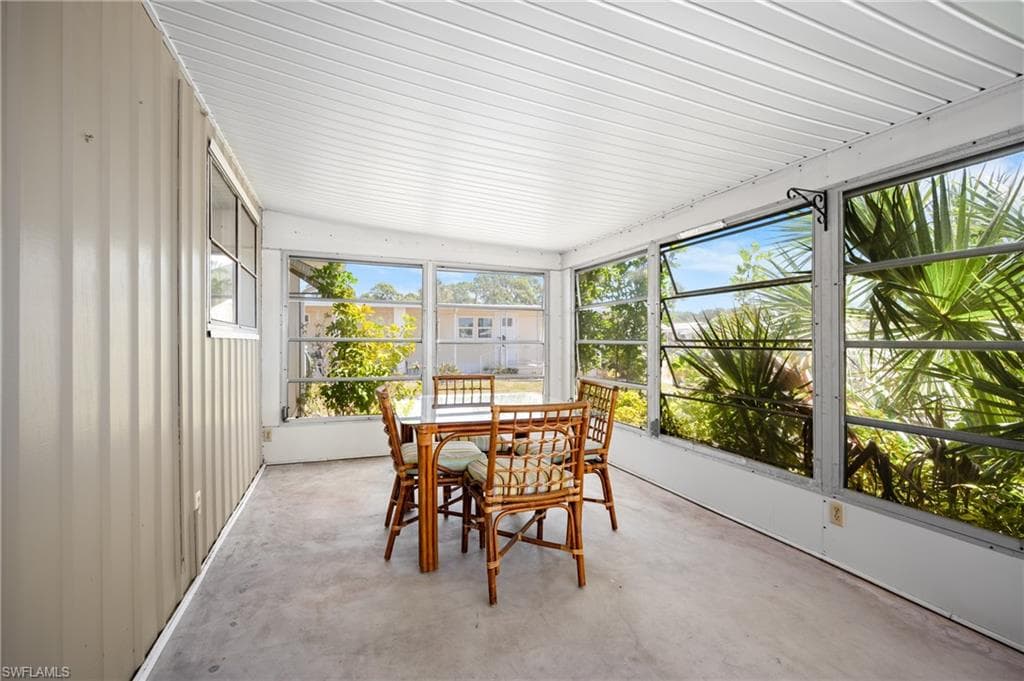 Screened-in porch featuring a corrugated panel ceiling, multiple glass pane windows, a concrete floor, and a corrugated panel wall