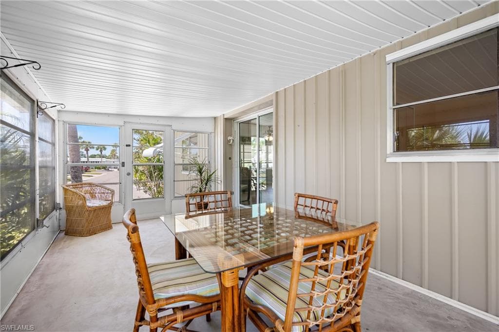 Enclosed sunroom featuring a white paneled ceiling, light-toned concrete flooring, large screen windows, a full-light screen door, and vertical panel siding