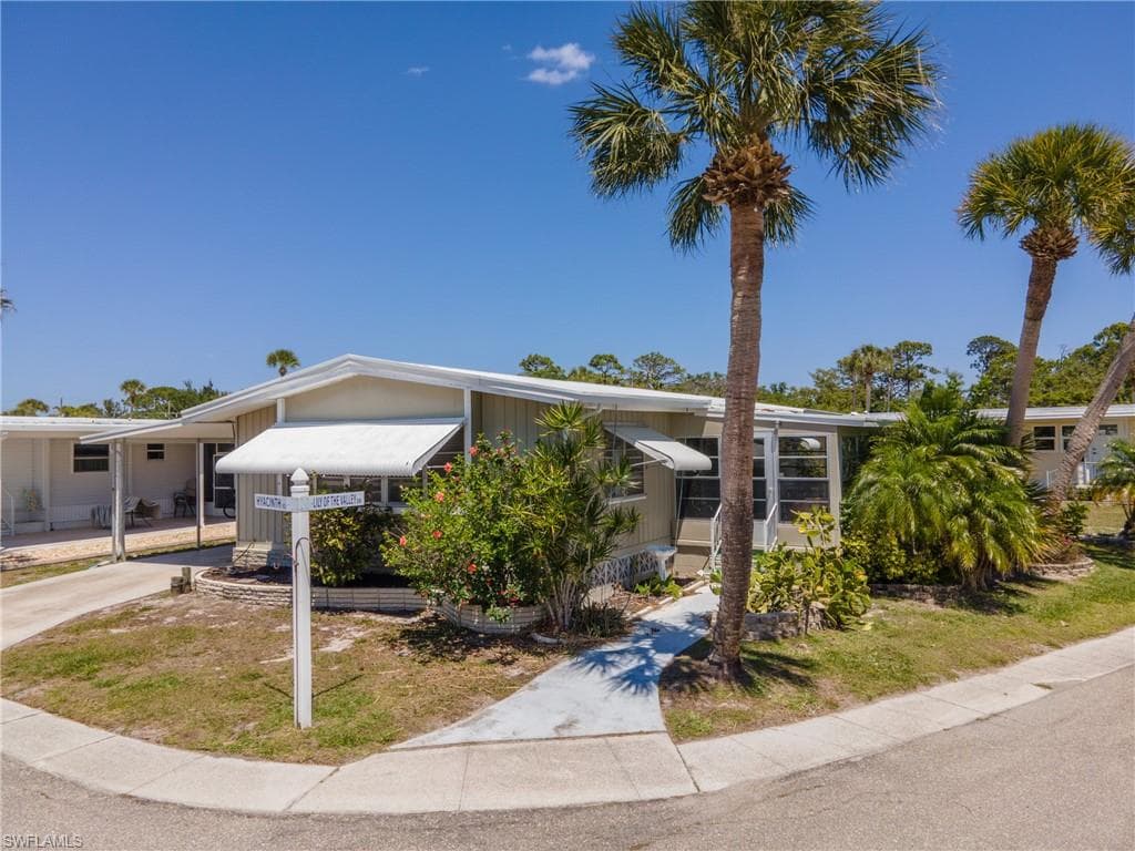 Single-story residence featuring a carport, mature palm trees, and established landscaping