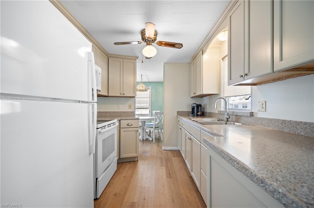 Galley kitchen featuring wood-finish flooring, white appliances, light-toned cabinetry, and speckled countertops