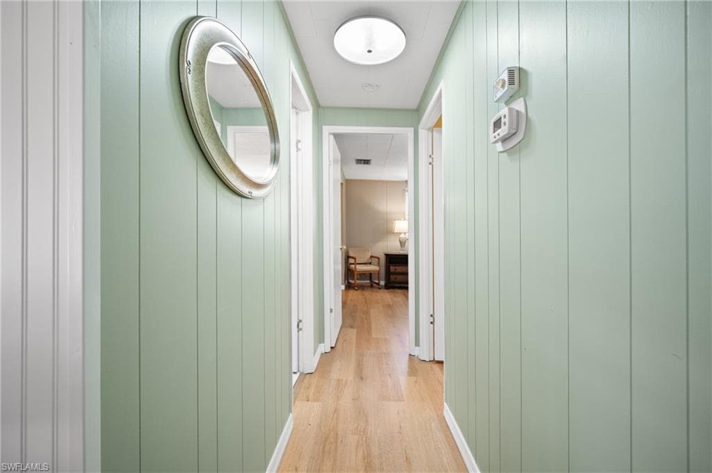 Hallway featuring vertical paneling walls, wood-finish flooring, white trim, and flush-mount lighting