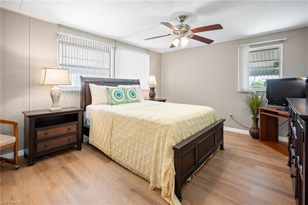 Bedroom featuring light wood-finish flooring, a ceiling fan with integrated lighting, and vertical paneling on walls