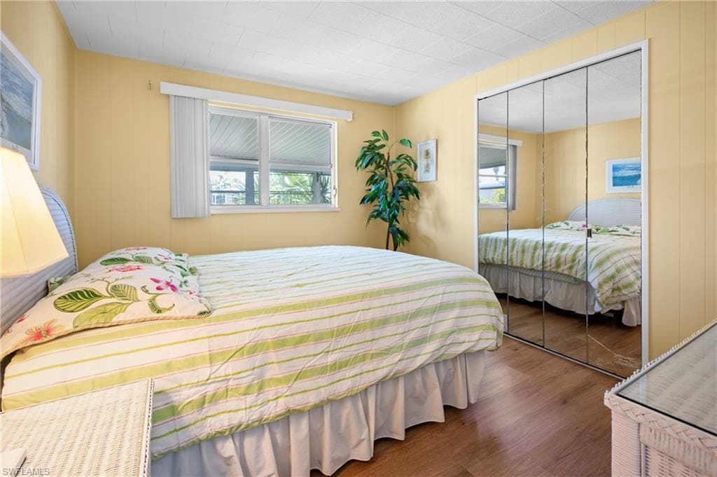 Bedroom featuring wood-finish flooring, a double window with blinds, and mirrored sliding closet doors