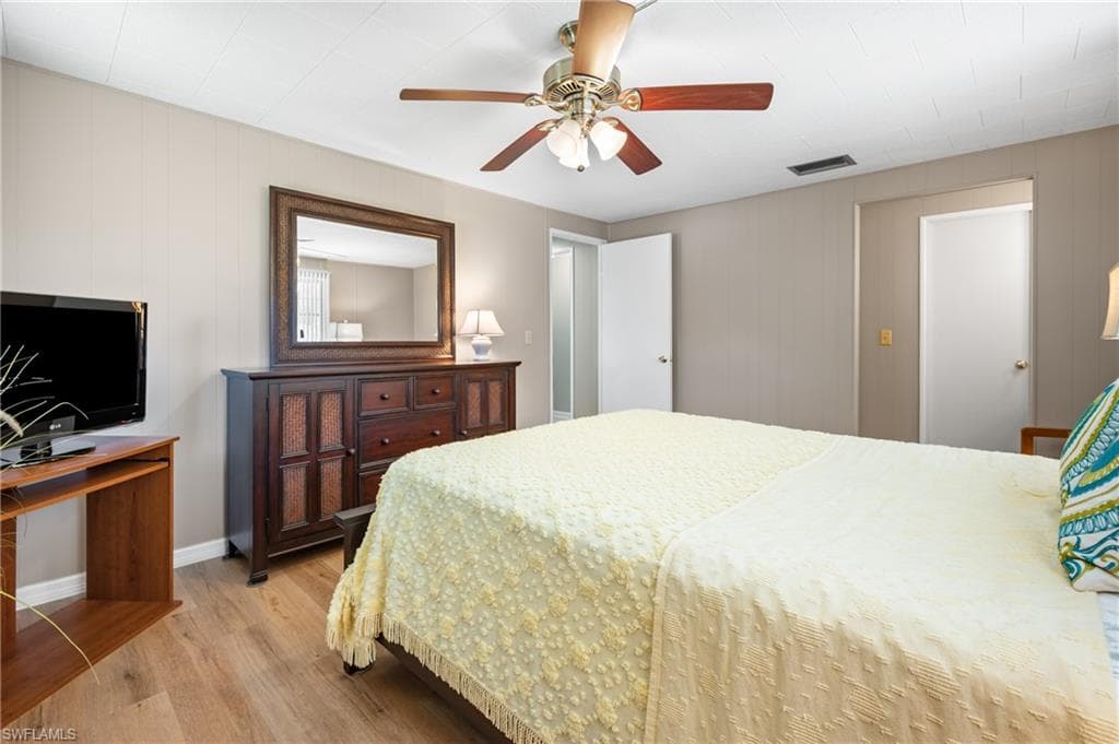 Spacious bedroom featuring wood-finish flooring, a ceiling fan with light fixture, and neutral wall tones