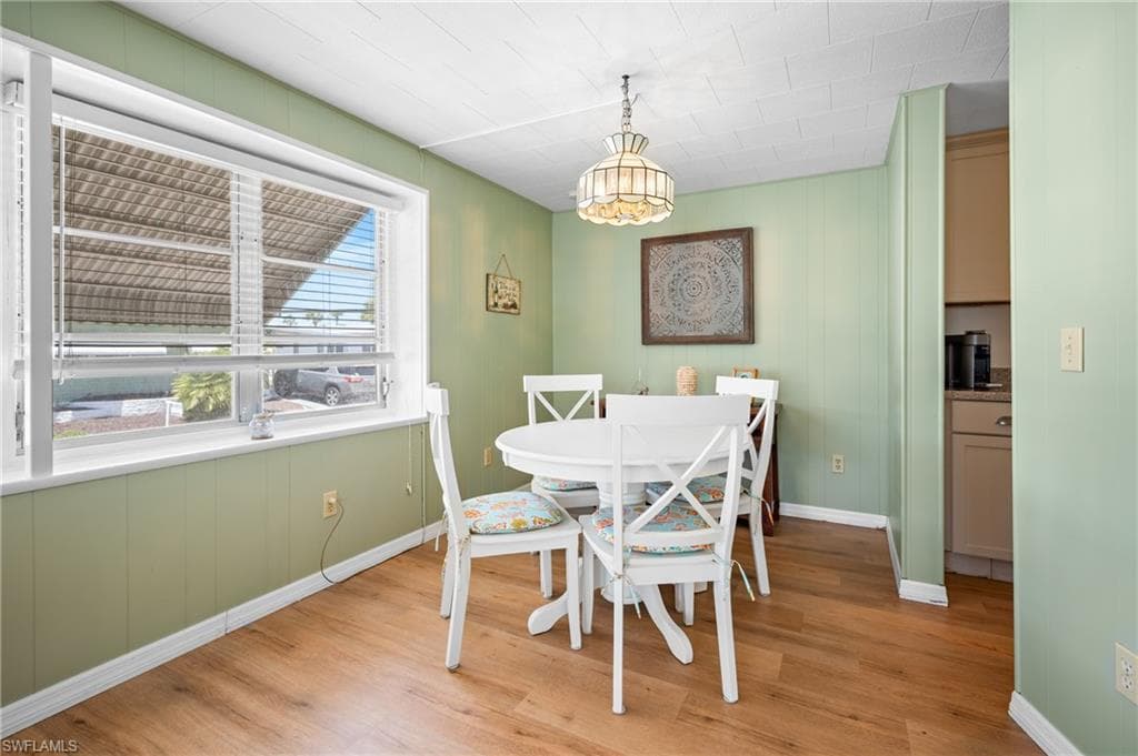Dining area featuring wood-finish flooring, a large window with blinds, paneling, and a chandelier