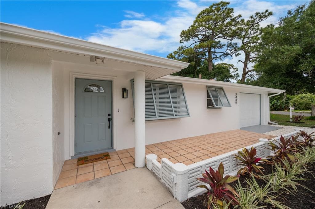 White stucco exterior with a light blue entry door, featuring a tiled front patio and decorative landscaping