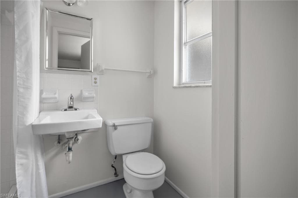 Compact bathroom featuring a wall-mounted sink with chrome faucet, a toilet, and a frosted glass window