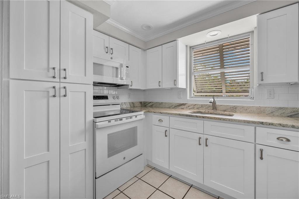 Kitchen featuring white shaker-style cabinetry, granite countertops, subway tile backsplash, and a white appliance suite