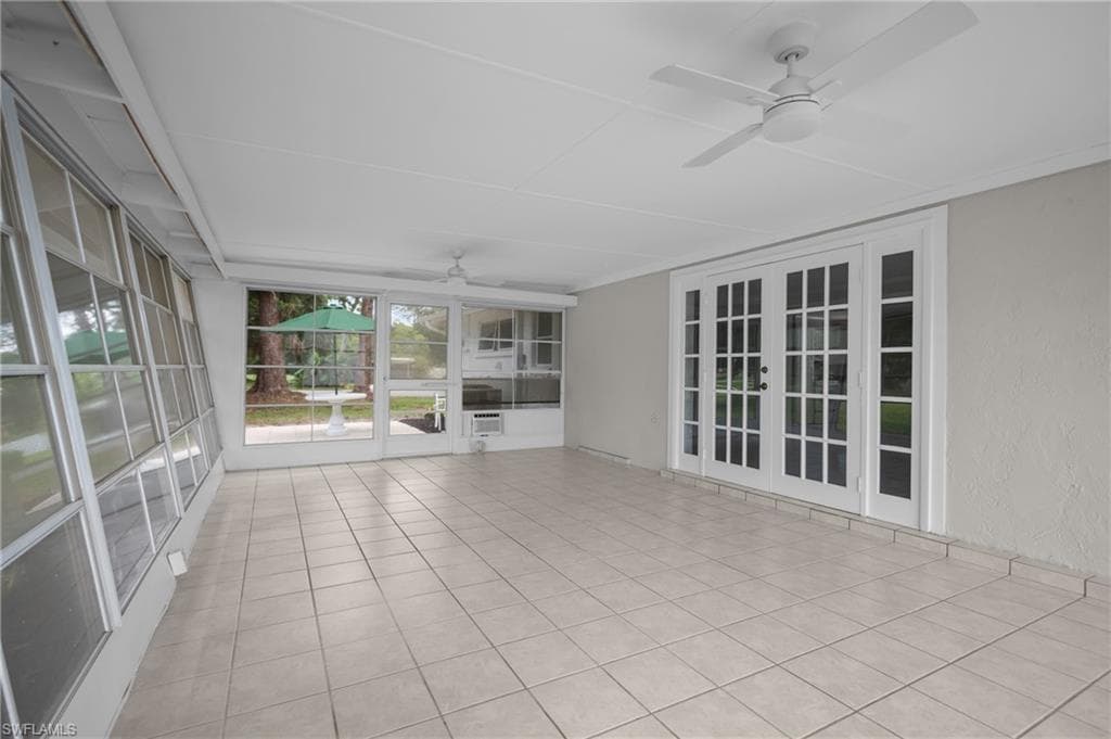 Spacious sunroom featuring light-toned tile flooring, dual ceiling fans, multiple window panels, and French doors