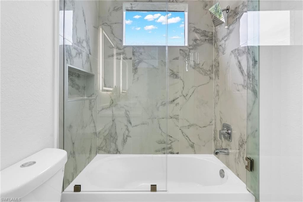 Bathtub and shower combination featuring white marble-patterned tile, a clear glass enclosure, and a built-in shower niche